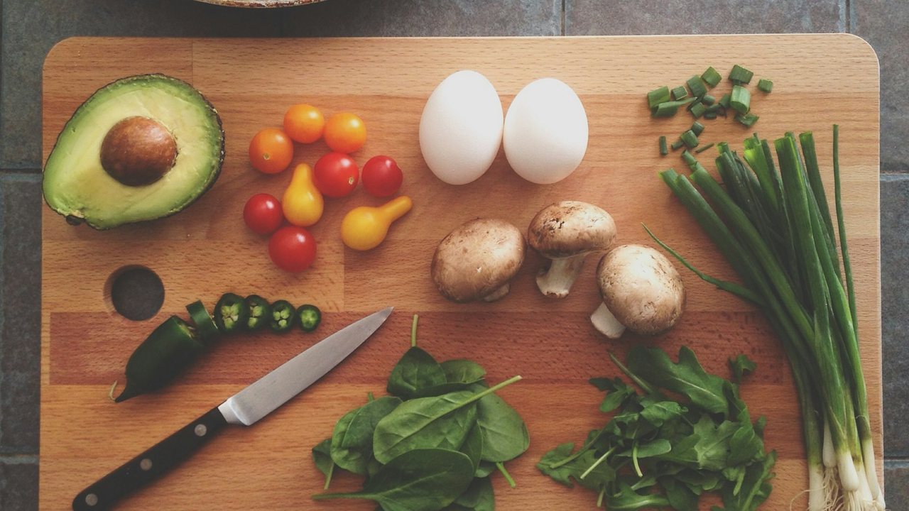 Eggs, greens, and vegetables laid out on a wooden cutting board
