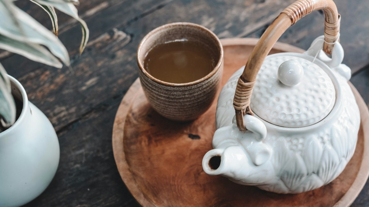 White teapot and cup of tea on a wooden tray
