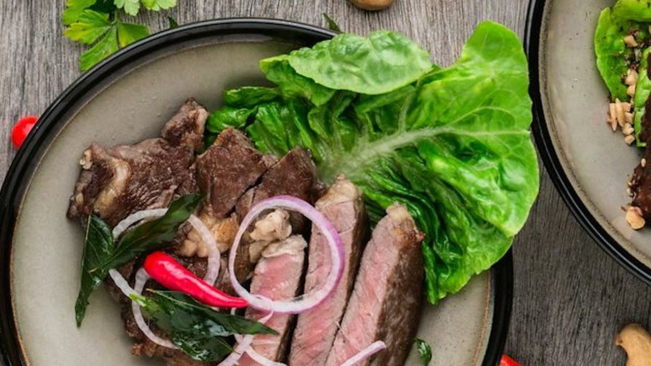 Sliced seared beef with lettuce, red onion, and chili on a dark plate